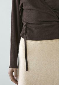 Brun langærmet omslagstop med bindedetalje kombineret med en lysebeige strikket nederdel med ribbede taljebånd og blød tekstur.