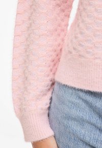 Pull en maille rose clair texturée avec un motif à bulles, finition douce et poignets côtelés, associé à un denim bleu.