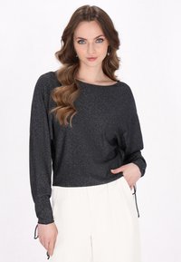 Zwarte, sprankelende blouse met lange mouwen, een brede halslijn en een geplooide accent aan de zijkant, gecombineerd met lichtgekleurde, losse broek.