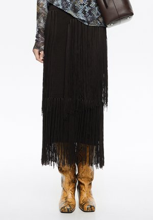 Czarna spódnica z frędzlami o fakturowanym splocie, zestawiona z brązowymi kowbojkami ze skóry węża. Strój wyróżnia się warstwowanymi wzorami i akcentami.