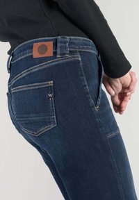 Jeans i mörkblå denim med en brunt läderlappar med en cirkellogo på baksidan, fem fickor och diskreta sömdetaljer.