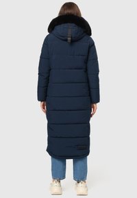 Marineblauer langer Puffermantel mit einem plüschigen schwarzen Pelzkragen, horizontalen Steppnähten und einem Logo-Patch. Er verfügt über eine Kapuze und lange Ärmel.