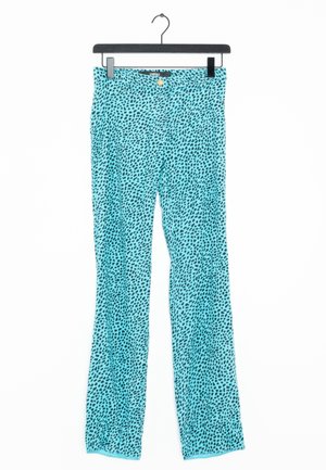 Pantalon turquoise à jambes droites avec un motif de points noirs irréguliers, bouton doré et étiquette VERSACE, suspendu sur un cintre noir.
