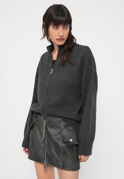 Sweater cinzento escuro com fecho de correr, em tecido de malha suave, apresentando uma gola alta e um corte largo, combinado com uma mini saia de couro preta com fecho de correr frontal.