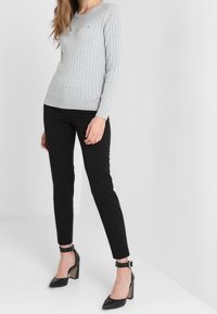 Maglione grigio a coste con maniche lunghe, abbinato a pantaloni neri aderenti e scarpe col tacco nere con cinturini alla caviglia. Design semplice e pulito.