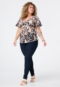 Blusenshirt mit floralem Muster, kurzen Ärmeln in Hellrosa und Schwarz, mit einem schmeichelnden V-Ausschnitt und Knoten-Detail, kombiniert mit dunklen Skinny Jeans.