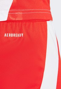 Rode sportieve shorts met witte accenten, gemaakt van een gladde, ademende stof. "AEROREADY" logo gedrukt in het wit. Zichtbare stikdetails.