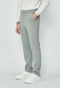 Pantalon de sport gris clair avec une taille élastique, poches latérales, coupe droite et texture lisse. Assorti à des baskets blanches.