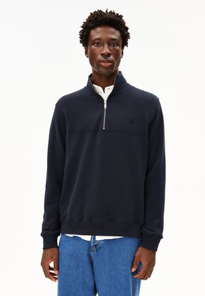 Sweat-shirt bleu marine à col zippé et poignets côtelés. Présente un petit logo sur la poitrine et un tissu au toucher lisse.