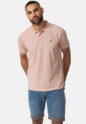 Polo skjorte, lyserødt stof med en struktureret finish, tre-knaps lukning, kontrasterende hvid krave, broderet logo på brystet, parret med denim shorts.