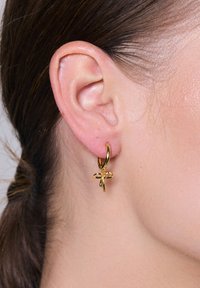 Złote kolczyki w kształcie obrączek z wisiorkiem w kwiatowym wzorze, gładka faktura z błyszczącym wykończeniem oraz małe ozdoby na środku.