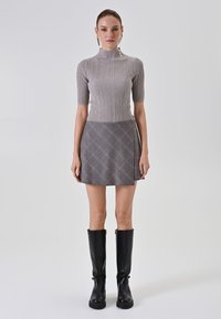 Top grigio a righe con maniche corte e dettagli a bottoni, abbinato a una mini gonna a quadratini grigia. Stivali neri fino al ginocchio con un leggero tacco.