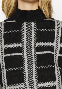 Czarny sweter dziany z wysokim kołnierzem, ozdobiony geometrycznym wzorem w odcieniach szarości. Teksturowana powierzchnia z naprzemiennymi wzorami w blokach i paskach.