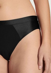 Zwarte bikini slipjes met een gladde textuur, voorzien van een brede, licht glanzende tailleband en een minimalistisch design.