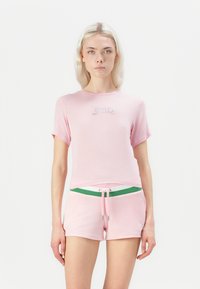 Rozā īso piedurkņu tops ar uzrakstu "Juicy" sudraba rhinestones, savienots ar rozā šortiem ar zaļu savilcēju un jostasvietu.