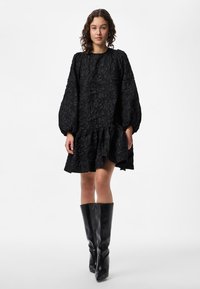 Crna haljina s teksturom, s puf rukavima i volanima na rubu. Do koljena, uparena s crnim čizmama do koljena, glatke završne obrade.