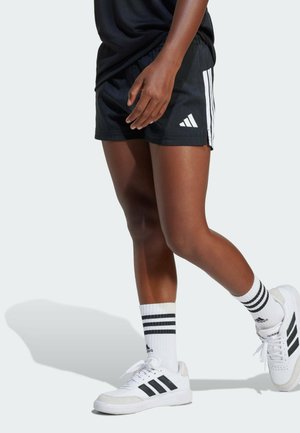 Černé sportovní šortky s třemi bílými pruhy po stranách, doplněné bílými teniskami a pruhovanými ponožkami. Šortky mají elastický pás.