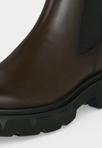 Καφέ δερμάτινη μπότα Chelsea με μαύρο ελαστικό πλαίσιο στο πλάι και χοντρή μαύρη σόλα με ανάγλυφα πέλματα.