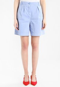 Světle modré upravené šortky s plisováním, zapínáním na knoflík a ohrnutým lemem. Vyrobené z hladkého materiálu, doplněné červenými špičatými podpatky.