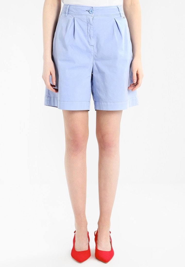 Světle modré upravené šortky s plisováním, zapínáním na knoflík a ohrnutým lemem. Vyrobené z hladkého materiálu, doplněné červenými špičatými podpatky.