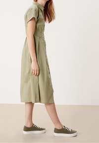 Košilové šaty s krátkým rukávem v světle olivově zelené barvě, s přiléhavým korzetem a rozšířenou sukní. V kombinaci s tmavě zelenými teniskami.
