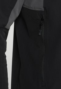 Svart jacka med en slät textur, kontrasterande grå detaljer, framdragkedja och en vinklad sidofickdesign.