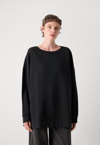 Črni oversize sweatshirt z širokim izrezom, dolgimi rokavi in mehkobo teksturo. Ima ribane manšete in sproščen silhueto.