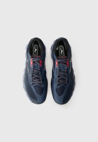 Baskets de sport bleu marine avec une tige texturée, dotées d'accents rouges, de lacets gris et d'une semelle rembourrée. Design épuré avec logo.