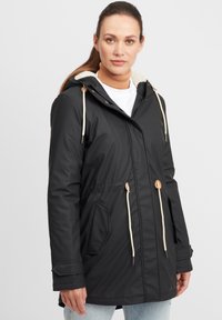 Zwarte waterdichte jas met een capuchon, beige voering, toggles en voorzakken. Kenmerkt een aangesnoerde taille en gestructureerde stof.