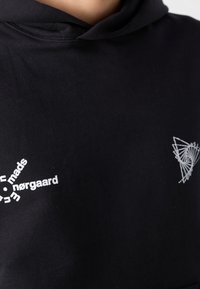 Sweat à capuche noir avec un logo géométrique abstrait blanc et un design de texte circulaire sur la poitrine.