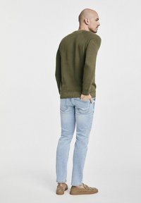 Olive zielony sweter dzianinowy o żebrowanej strukturze, jasnoniebieskie dżinsy i beżowe buty wsuwane, widok z tyłu.