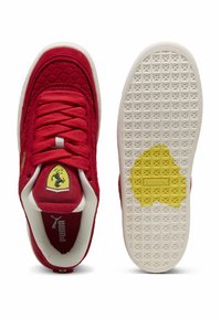 Sarkani zamšas sporta apavi ar dimanta rakstu augšdaļā, baltu gumijas zoli, dzeltenu Puma logotipu uz zoles un Ferrari emblēmu uz mēles.