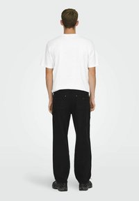 Witte t-shirt met korte mouwen, losse zwarte cargo-broek met zakken en zwarte sneakers, gezien van achteren.