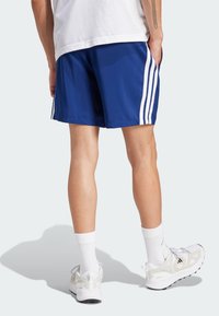 Blauwe sportshorts van gladde stof, met witte verticale strepen aan de zijkanten, gecombineerd met witte crew-sokken en sneakers.