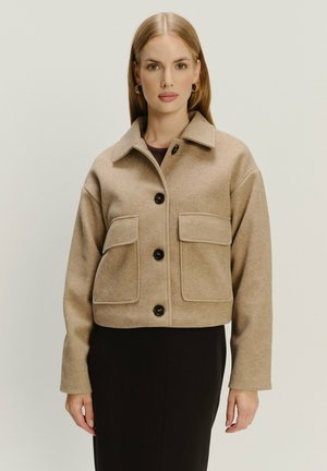 Afgeknot beige wollen jas met een knoopsluiting, twee voorzakken en een klassieke kraag. Beschikt over zwarte knopen en een gladde textuur.