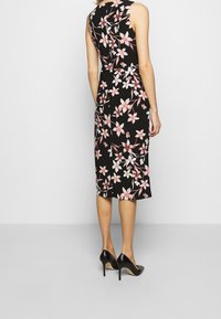 Svart blommig klänning med rosa och vita blomstertryck, ärmlös design, knälång, kombinerad med svarta högklackade skor.