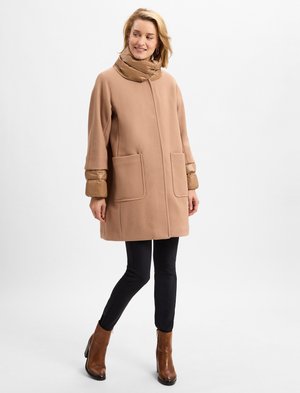 Cappotto in misto lana marrone con ampie tasche frontali, colletto alto in tessuto trapuntato, abbinato a pantaloni neri e stivaletti a tacco marroni.