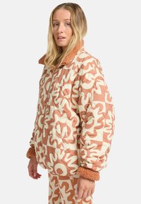Gevoerde jas in crème met abstracte oranje patronen. Bevat een zachte, bruine, nepbont kraag en manchetten. Voorzijde met ritssluiting.