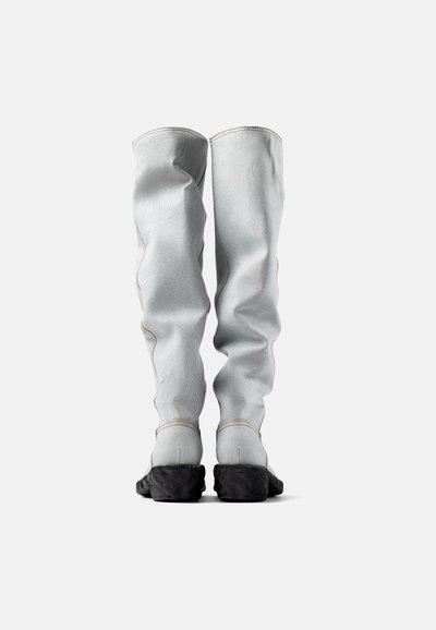 Botas grises hasta el muslo con un upper suave y texturizado y suelas de goma con un diseño robusto. Costuras en contraste a lo largo de las costuras.