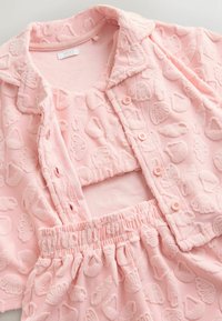 Ensemble en tissu rose texturé comprenant une chemise boutonnée, un top court et un short à taille élastique avec motif coquillage embossé partout.