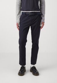 Marintröjor med slim fit, bälte med fem silverösehål, ihopparat med en mörk överdel och randig långärmad skjorta; bärs med svarta skor.