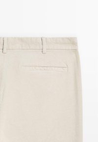 Beige corduroy pants featuring a smooth texture, discreet back pocket, and belt loops; designed for a fitted silhouette and casual wear.