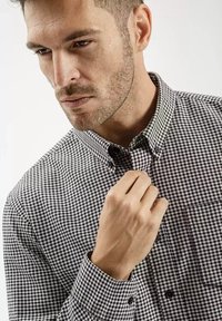 Czarna i biała koszula w kratę z guzikami, z kołnierzykiem, długimi rękawami i kieszenią na piersi; materiał ma gładką strukturę i dopasowany fason.