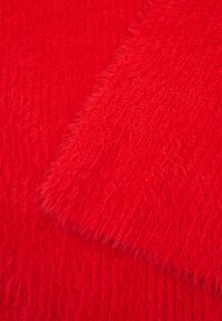Rode gebreide stof met een fluffy textuur. Het oppervlak toont een mix van gladde en gestructureerde secties met een consistente dieprode kleur.
