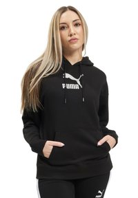Čierna mikina s kapucňou z mäkkej látky, s kloktanou vreckom, šnúrkami a bielym logom Puma na hrudi. Jednoduchý, voľný strih.