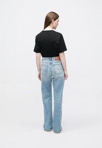 Zwart T-shirt met korte mouwen gecombineerd met lichtblauwe, hooggesneden spijkerbroek. De jeans hebben een klassieke vijfzakkenconstructie en een leren merkembleem.