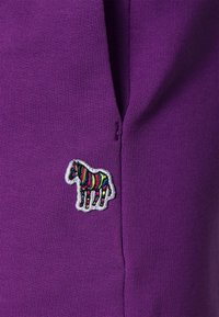 Lila Stoff mit einem strukturierten Strickmuster, das einen kleinen, bunten, bestickten Zebra-Patch an der Seite zeigt.