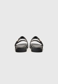 Svarta sandaler med två breda remmar, platt sula och en texturerad innersula. Har en liten guldfinish på remmarna. Minimalistisk design.