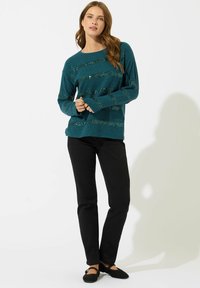 Maglione teal con strisce orizzontali di paillettes, scollatura rotonda e maniche lunghe, abbinato a pantaloni neri e scarpe flat nere.