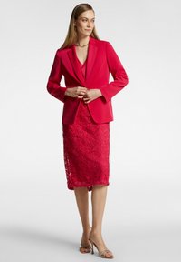 Blazer fucsia brillante con revers a punta, abbinato a una gonna in pizzo floreale a lunghezza ginocchio. L'abbigliamento presenta una finitura liscia e una texture sottile.